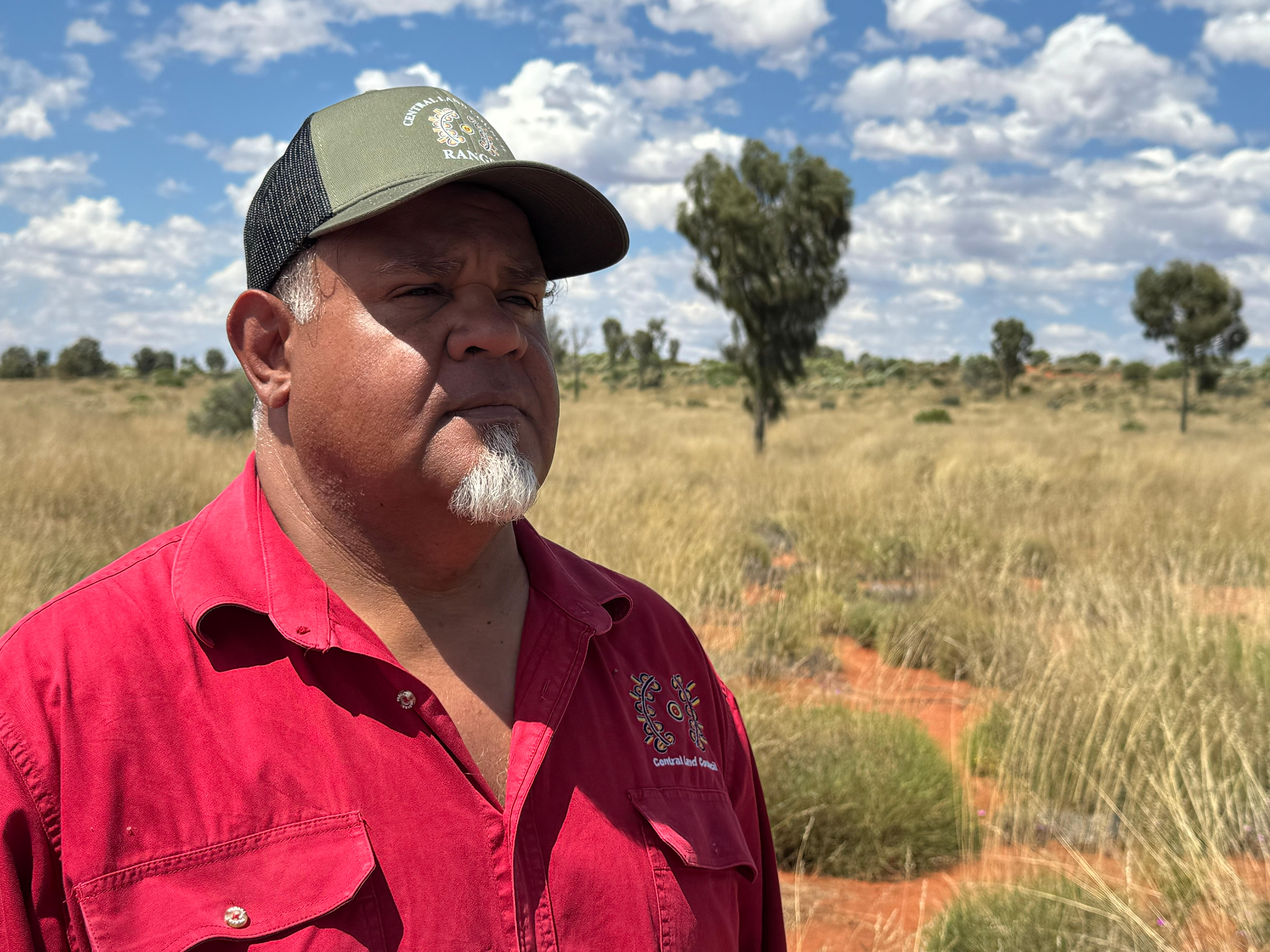 Garth Forrester stands in front of a scene of red dirt and dry scrub.