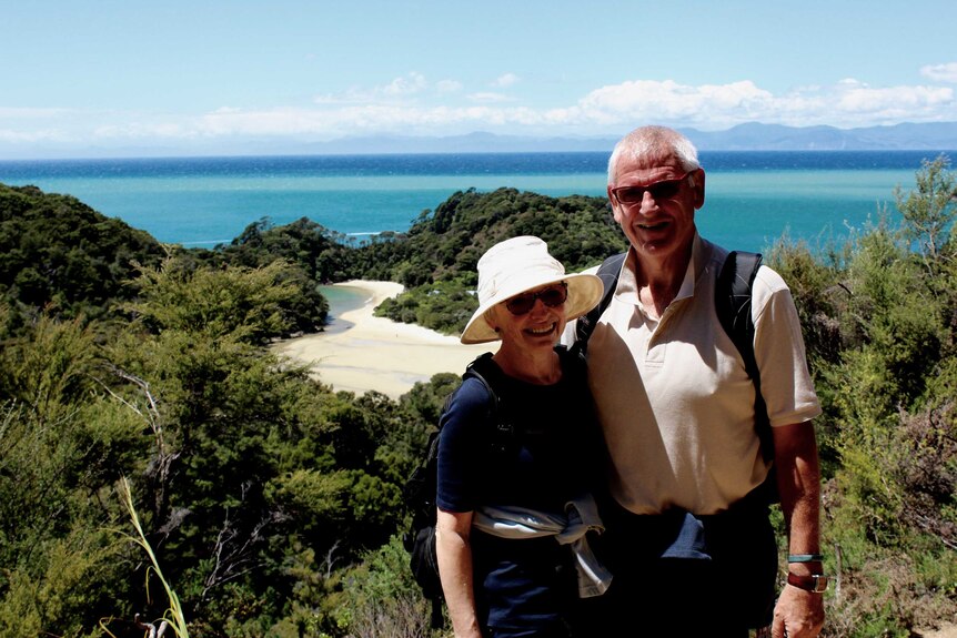 Helen and Ian Anderson stand with their arms around each other with a beach in the background.