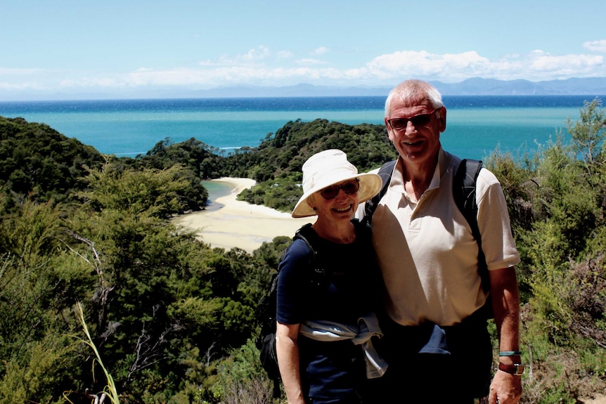 Helen and Ian Anderson stand with their arms around each other with a beach in the background.