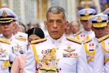 Thai King Maha Vajiralongkorn wears a decorative white and gold uniform and is walking in front of a large group of officials
