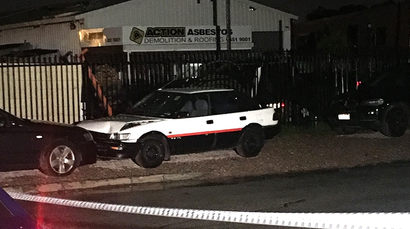 Night shot of an asbestos business with a damaged car parked out the front and police tape in the foreground.