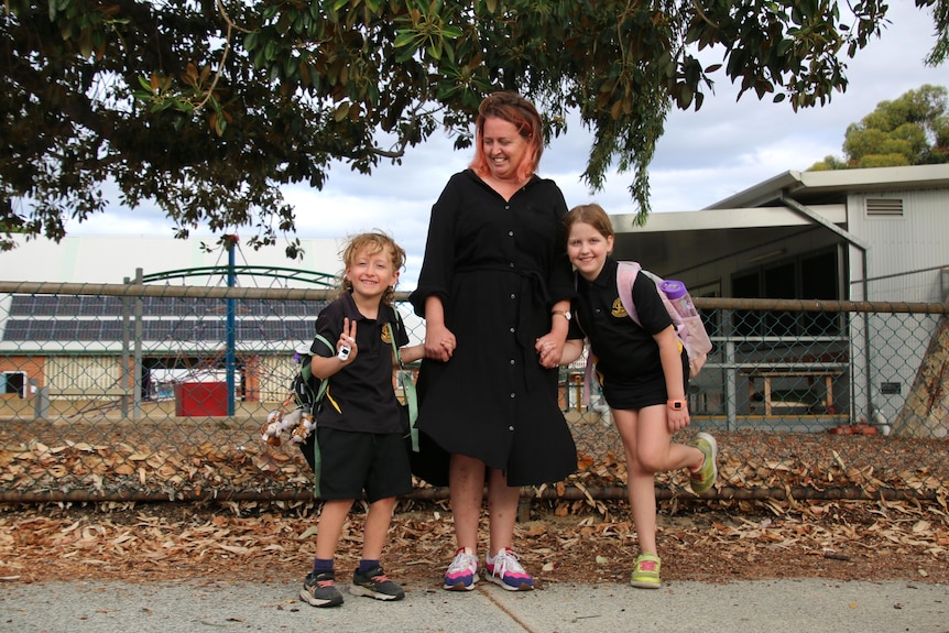 A woman named Myra Robinson flanked by two children in their primary school uniform. 