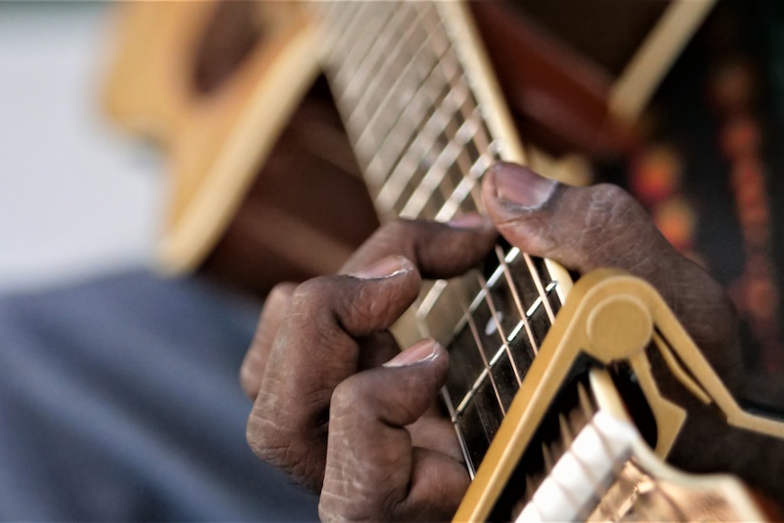 Close up of hands and capo on neck of guitar.