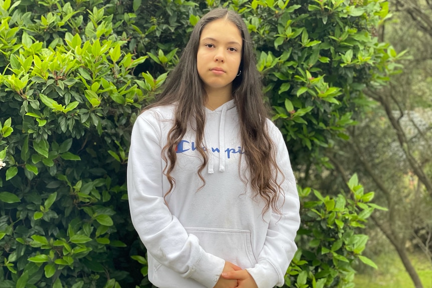 Scarlett Magnanini stands in front of a tree in a white sweatshirt and looks at the camera.