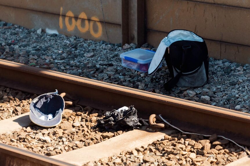 A bag, hat and other items strewn on train tracks.