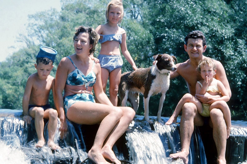 An old film photograph of the Hawke family sitting on a waterfall on a family holiday, smiling happily.