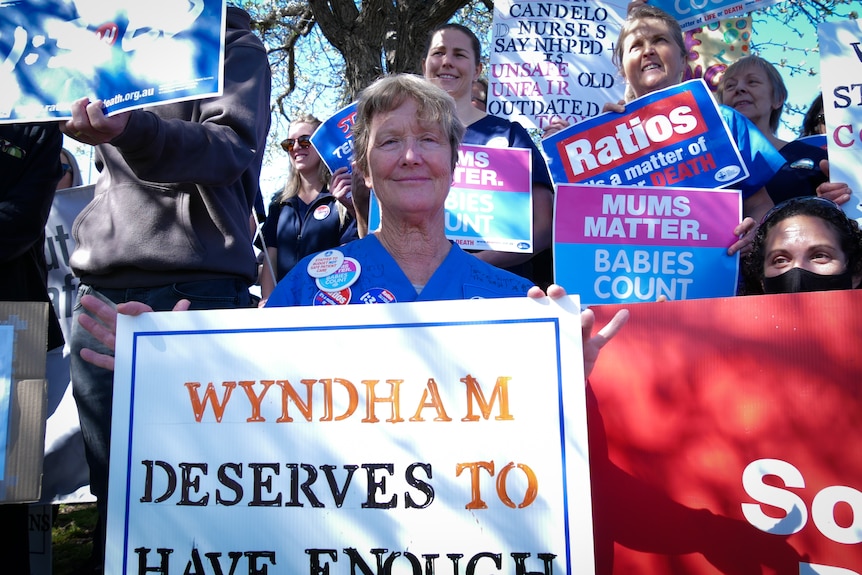 A nurse in her uniform holding a sign reading "Wyndham deserves to have enough"