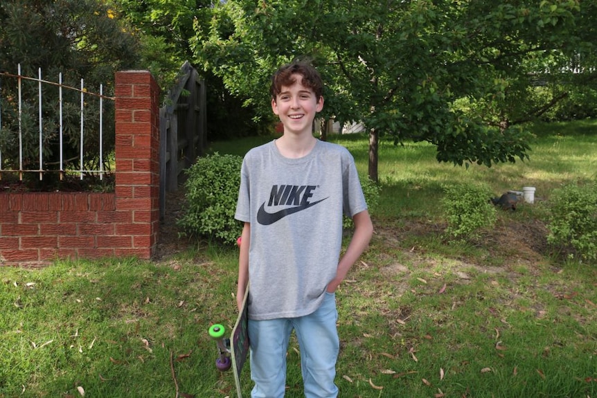 A young boy with a skateboard smiles outside