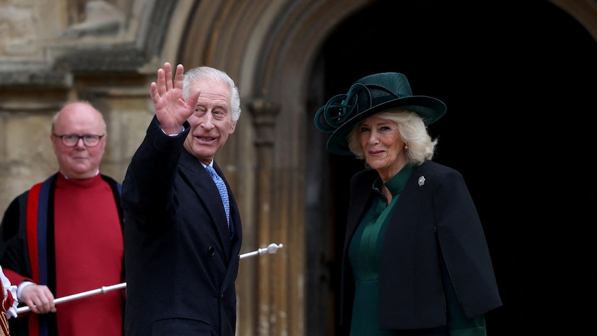 King Charles and Queen Camilla wave as they stand outside a church.