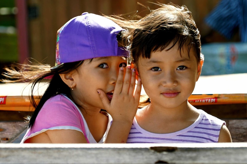 A little girl whispering into the ear of another little girl