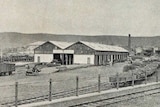 Black and white photo of an old goods shed with a railway line next to it 