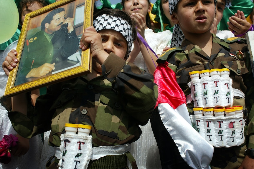 Boys dressed up as suicide bombers march in a parade.