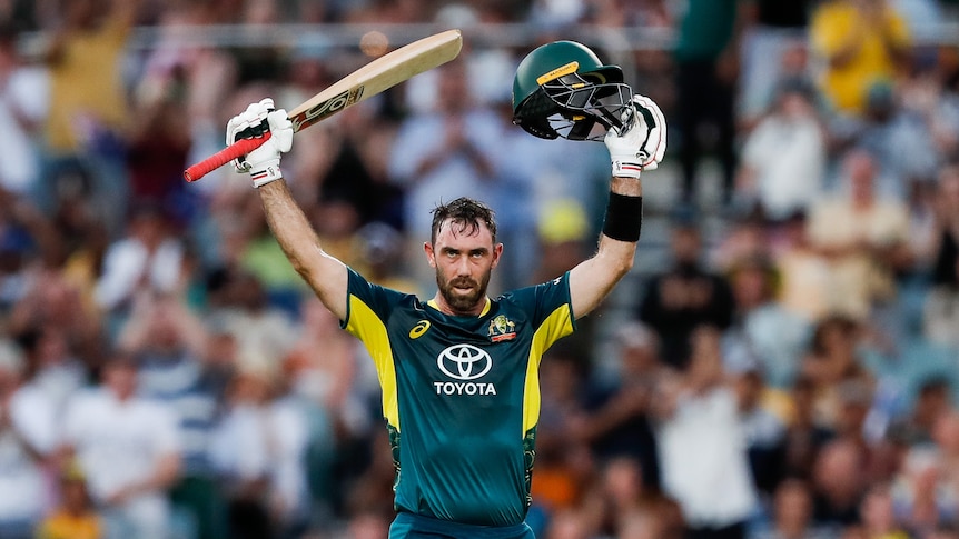 Glenn Maxwell with his arms raised holding a helmet and cricket bat. 