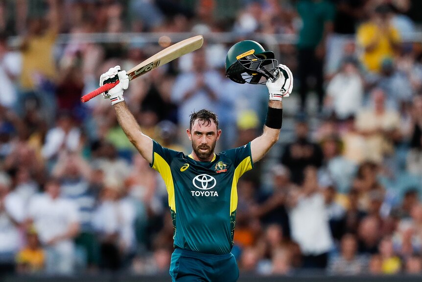 Glenn Maxwell with his arms raised holding a helmet and cricket bat. 