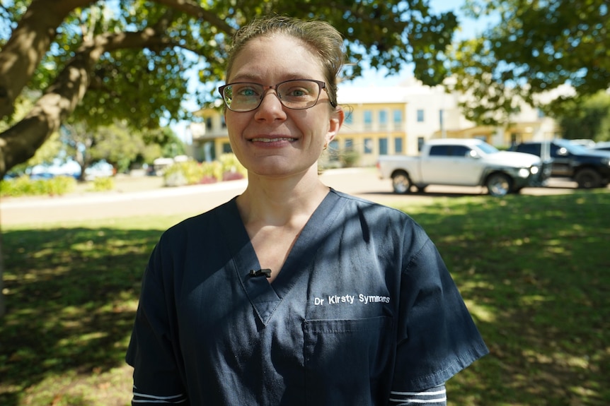 A woman in scrubs looks at the camera in front of the Longreach Hospital