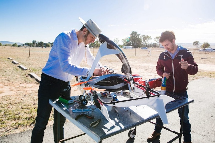 Two men look at a flight-capable scale model of a flying car