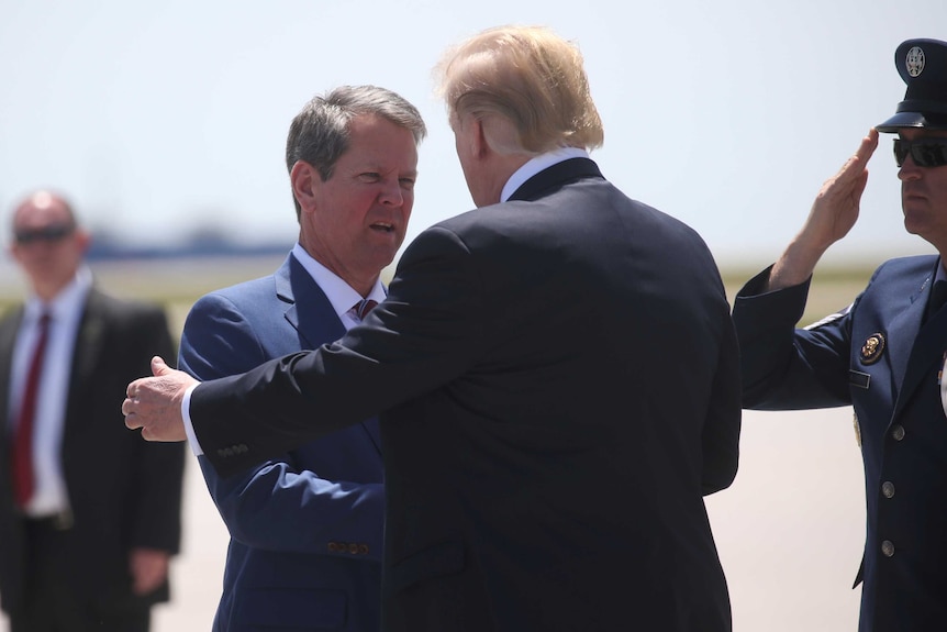 Donald Trump is seen from behind as he shakes a man's hand and pats him on the shoulder