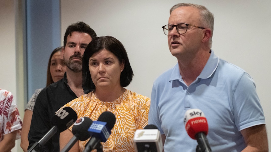 A man with dark-rimmed glasses speaks at a press conference next to a woman with dark hair