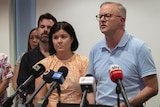A man with dark-rimmed glasses speaks at a press conference next to a woman with dark hair