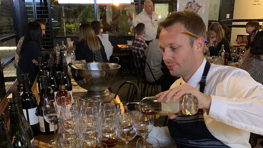 Clement Demarais pours glasses of wine in a restaurant.