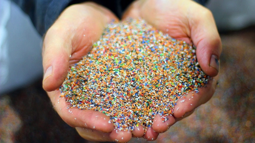 A man's hands cupped with multi-coloured plastic particles