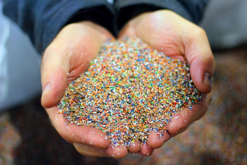A man's hands cupped with multi-coloured plastic particles