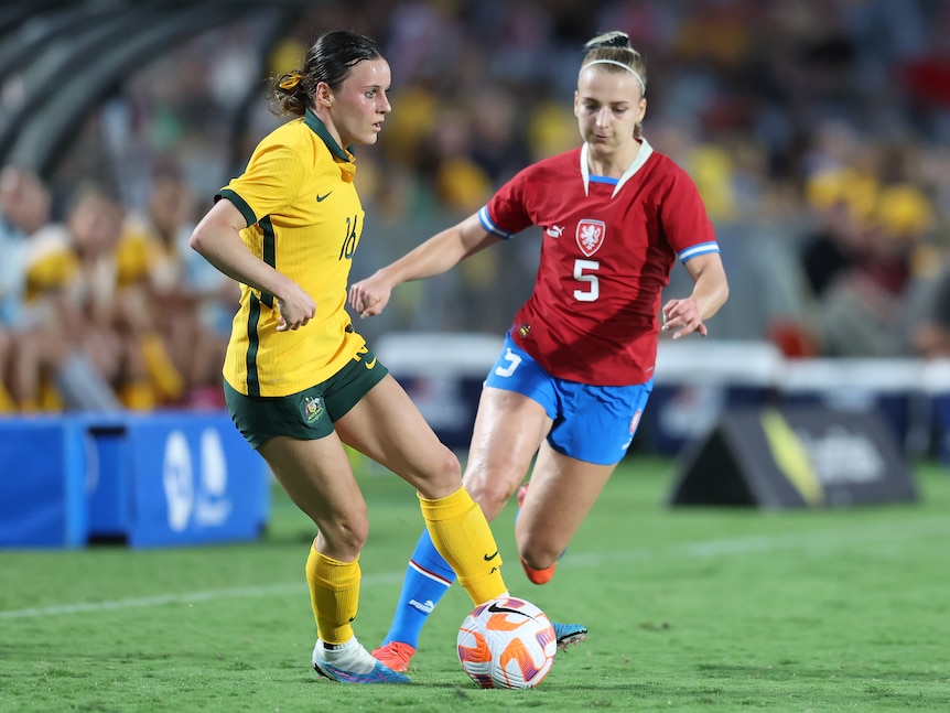 A soccer player wearing yellow and green playing a game against a player with red and blue clothes
