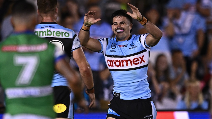 NRL player Daniel Atkinson of the Sharks raising his hands in the air, celebrating with a teammate.