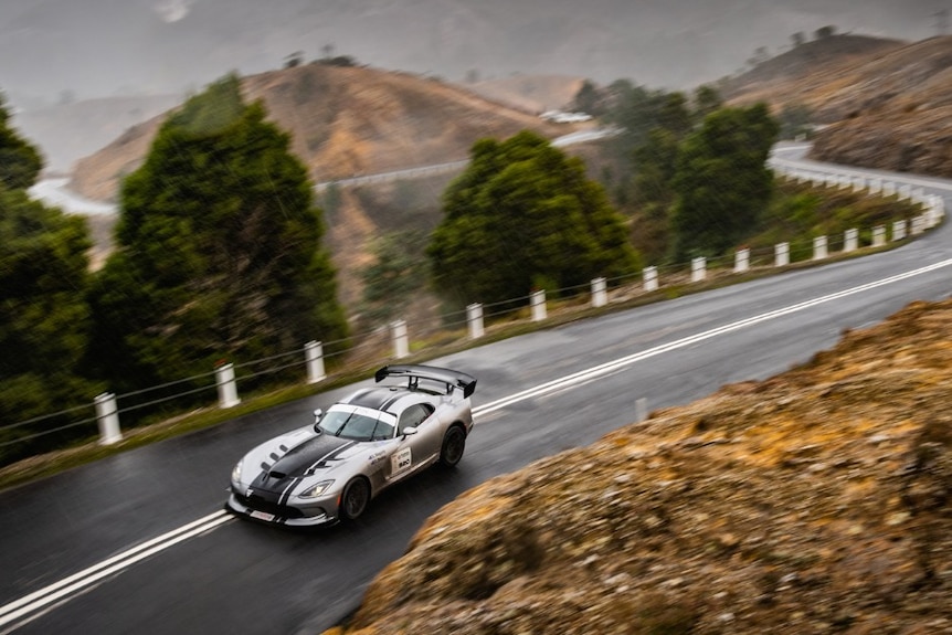 A silver racing car drives on a winding road