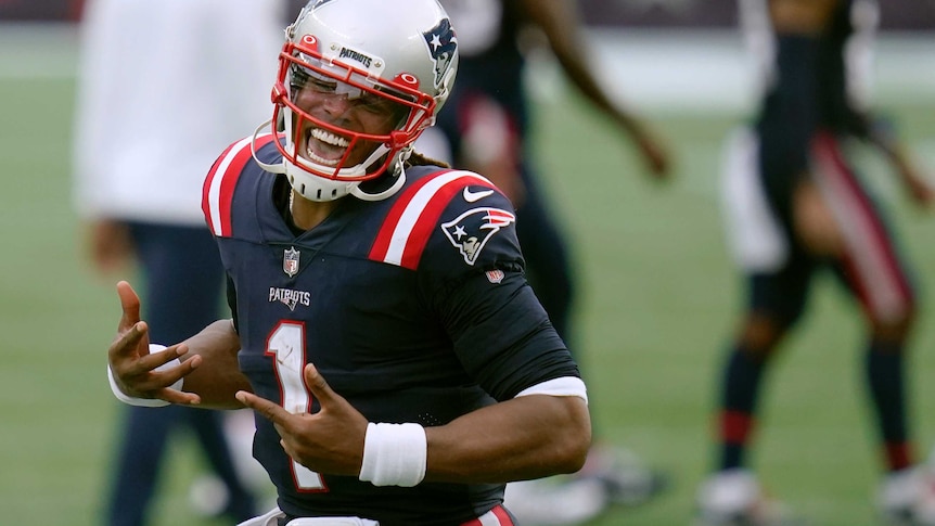 Cam newton smiles with his mouth wide open and holds his hands with fingers outstretched in front of him