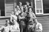 A black and white photo of a group of soldiers in uniform smiling in front of a weatherboard house.