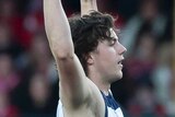 A male AFL player holds both arms in the air as he celebrates kicking a goal.
