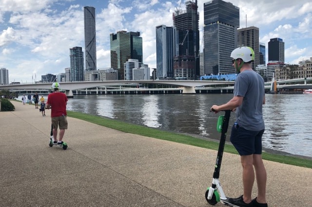 Two people ride Lime scooters along the Brisbane River.