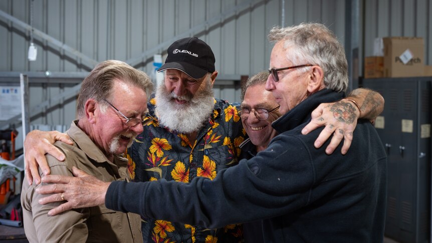 four men hug in a shed