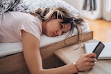 A woman in bed looks tiredly at her smart phone.