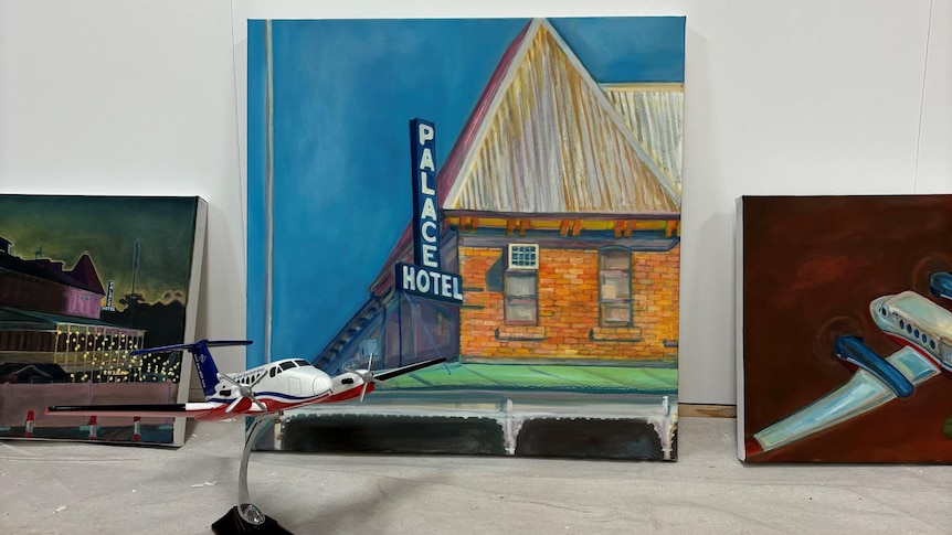 a model of a plane in front of three paintings, two of planes and one of a hotel