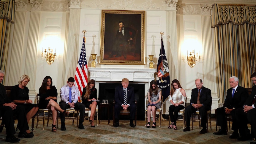 Donald Trump and students sit in a circle and bow heads during a prayer.