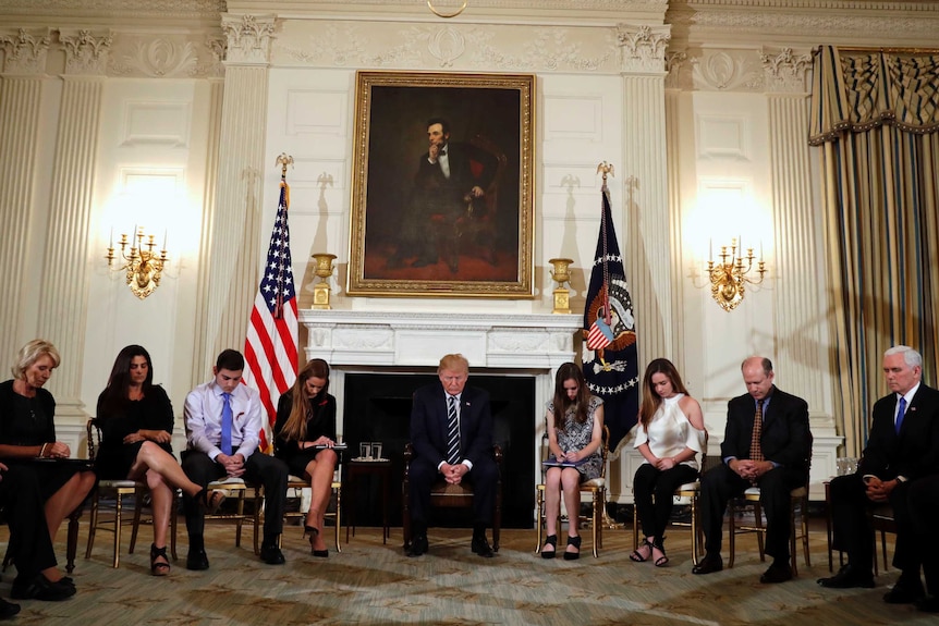 Donald Trump and students sit in a circle and bow heads during a prayer.