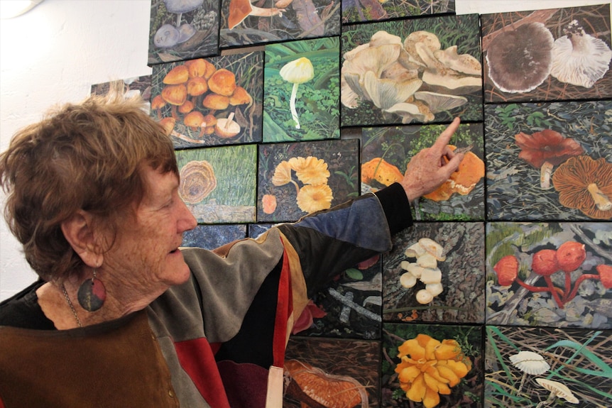 A woman points to a painting of a white sprawling mushroom. 