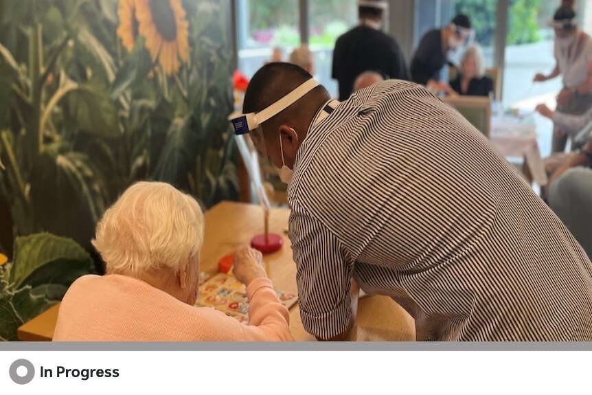 An aged care worker stands and attends to an elderly woman