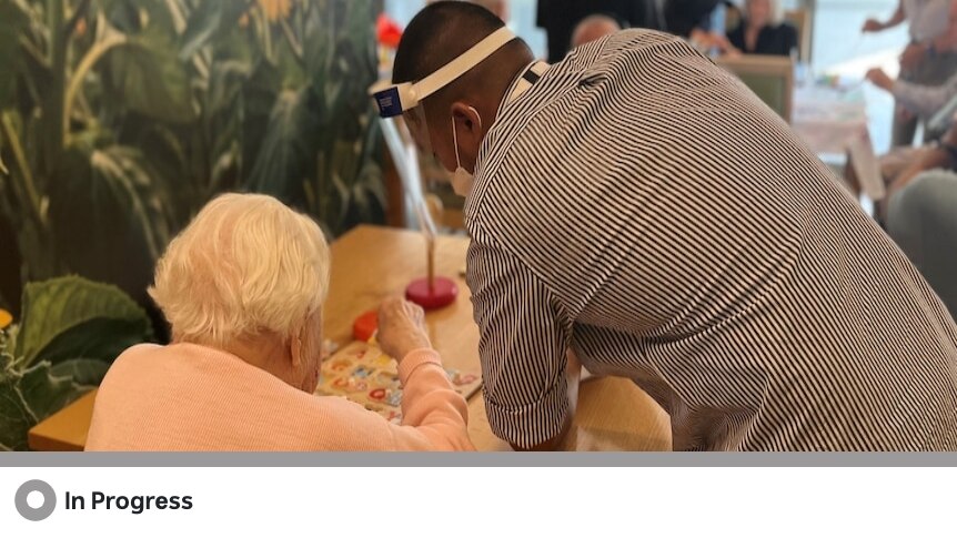 An aged care worker stands and attends to an elderly woman