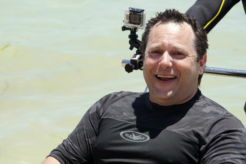 A man in a wet suit smiles at the camera