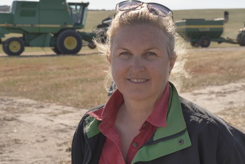 Blonde woman smiles in front of harvest machinery