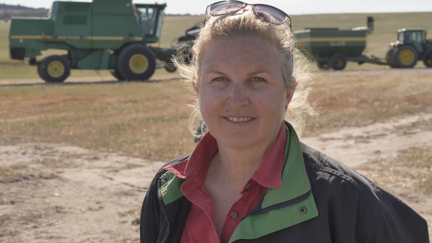 Blonde woman smiles in front of harvest machinery