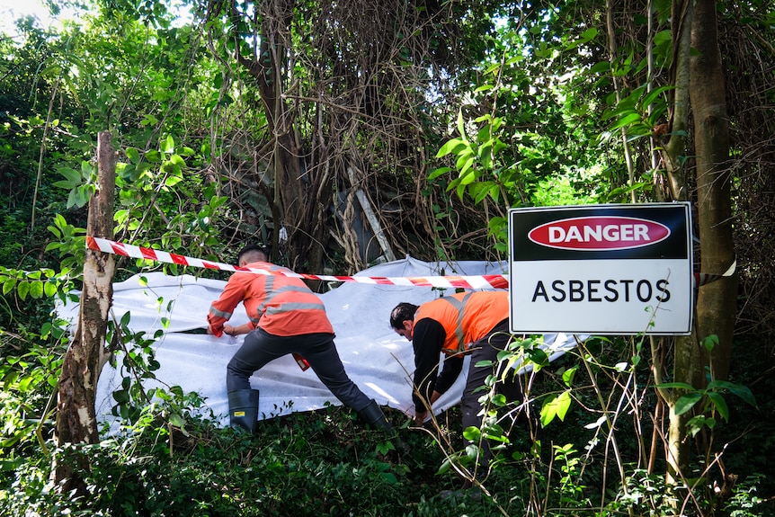 Men in high-vis workwear crouch over a white tarp being stretched over building materials