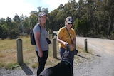 two women and their dog are searching in dense bushland