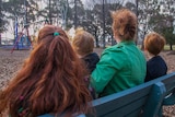 Back of the head shot of three children and a woman, all with red hair, sitting on a park bench