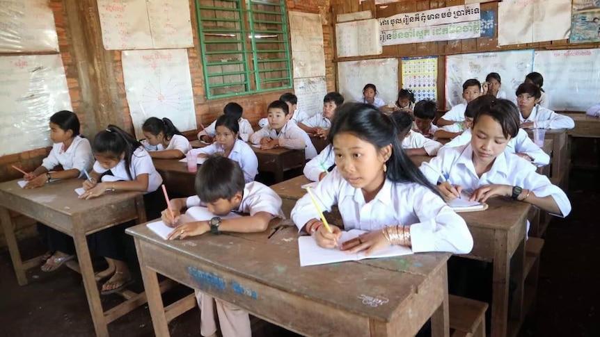 Boys and girls sit behind desks writing with pens and paper
