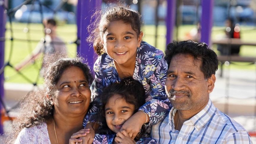 A mum and dad with two young daughters in front of a playground.