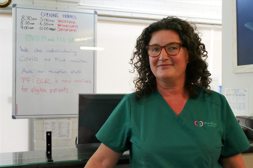 A woman stands in green medical scrubs in front of an office reception desk